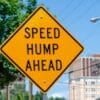 a yellow speed hump sign sitting on the side of a road