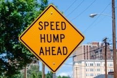 a yellow speed hump sign sitting on the side of a road